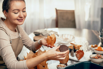 Wall Mural - A young woman packs cupcakes in a craft. concept of food delivery. A birthday package. small business. bakery chef bakes pastries and cakes in kitchen, copy space