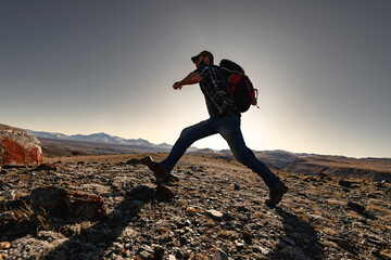Wall Mural - active hiker of tourist with a backpack accelerates before jumping in sunset mountains