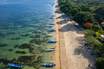 Wall Mural - Drone view of lines of traditional outrigger boats off a sandy tropical beach (Sanur, Bali)