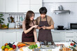 Portrait of young Asian couple male man female woman cheerful standing and preparing food for meal, enjoy cooking, in kitchen at home. Reading recipe in tablet.