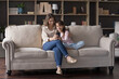 © fizkes - Mother and daughter using smartphone sit on couch in living room, staring at device screen enjoy videocall via apps, watch funny videos, spend carefree weekend leisure on internet. Modern tech usage