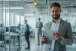 © ty - Handsome businessman using his tablet in the office, in the background are blurred employees working at their computers