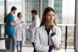 © fizkes - Serious pensive head doctor woman in white uniform standing in hospital hall space, touching chin, looking at window away, thinking clinic management, medical profession