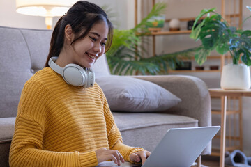 Beautiful young woman in a yellow casual dress enjoying listening to music and smiling while relaxing on the sofa at home. Young woman with headphones uses laptop and smartphone at home. relax concept