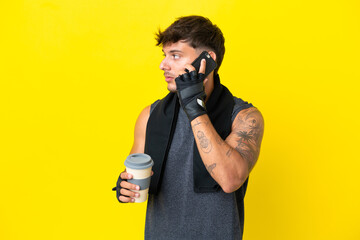 Young sport caucasian man with towel isolated on yellow background holding coffee to take away and a mobile