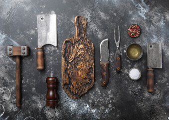 Wall Mural - Kitchen meat utensils set on dark plate background. Meat cleaver,fork,knife with wooden tenderizer and various herbs and oil.