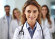 © DenisMArt - Beautiful young female doctor with stethoscope and doctors with nurses on the background.Macro.AI Generative.