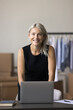 © fizkes - Portrait of middle-aged small business owner posing in warehouse. Female designer standing at desk with laptop at personal atelier workplace. Entrepreneurship, distribution, dropshipping, workflow