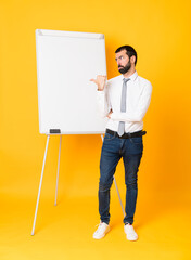 Wall Mural - Full-length shot of businessman giving a presentation on white board over isolated yellow background unhappy and pointing to the side