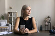 © fizkes - Pensive mature woman spend time at home, sit at desk hold mobile phone, looking away, wait call by business, send sms, chatting online, use gadget for communication, think about reply to text message