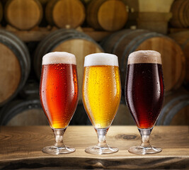 Canvas Print - Glasses of different chilled beer and wooden beer casks on the cellar background.