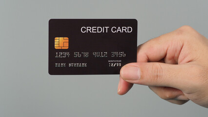 Wall Mural - Hand is holding black credit card isolated on grey background.