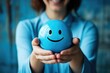 Woman holding blue smiley face in hands, expressing emotions, pretending emotions, depression, focusing on mental health, bringing you happiness