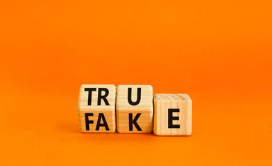 Wall Mural - Fake or true symbol. Turned wooden cubes and changed the word fake to true or vice versa. Beautiful orange table, orange background, copy space. Business and fake or true concept.