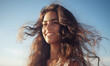 portret młodej brunetki z długimi włosami cieszącej się jasnym słońcem na tle błękitnego nieba