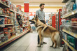 A man and a dog in a pet food store between shelves.