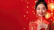 Happy Chinese new year. Asian woman holding angpao or red packet monetary gift and gold ingot isolated on red background.