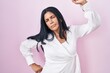 Mature hispanic woman standing over pink background stretching back, tired and relaxed, sleepy and yawning for early morning