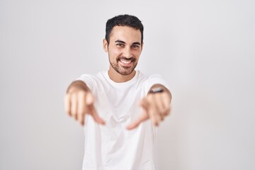 Sticker - Handsome hispanic man standing over white background pointing to you and the camera with fingers, smiling positive and cheerful