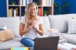 © Krakenimages.com - Young blonde woman studying using computer laptop at home praying with hands together asking for forgiveness smiling confident.