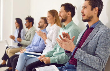 Diverse audience applauding at a business conference, lecture, or seminar. Young people with clipboards sitting in a row and clapping hands after listening to a speech by a talented business speaker