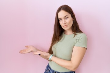 Wall Mural - Beautiful brunette woman standing over pink background inviting to enter smiling natural with open hand