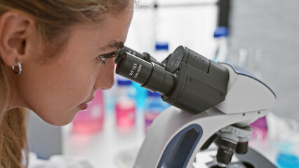 Poster - Dedicated young, beautiful blonde woman scientist engrossed in serious medical research, working with microscope at a bustling laboratory, injecting personality into the science of discovery