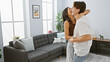 © Krakenimages.com - A delighted interracial couple embrace joyfully in a well-lit modern living room, expressing love and companionship.
