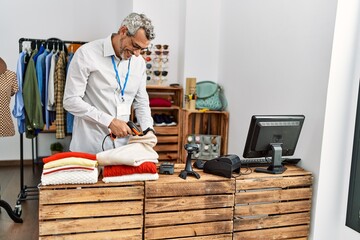 Poster - Middle age grey-haired man shop assistant scanning folded clothes at clothing store