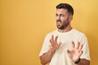 Handsome hispanic man standing over yellow background disgusted expression, displeased and fearful doing disgust face because aversion reaction.