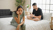© Krakenimages.com - Beautiful couple disagreeing in their bedroom, sitting on the bed, expressing conflict while using a smartphone, a problem causing a serious expression
