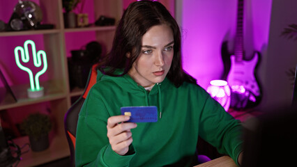 Canvas Print - A focused young woman holding a credit card indoors at night with colorful neon lights in a gaming room.