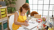 Mature woman artist sketching in a bright studio wearing an apron with art supplies around.