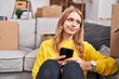 © Krakenimages.com - Young blonde woman using smartphone sitting on floor at new home
