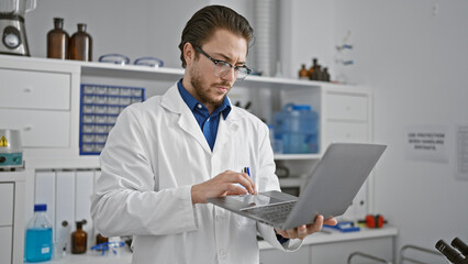 Wall Mural - Young hispanic man scientist using laptop at laboratory