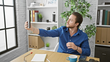 Wall Mural - Young hispanic man business worker make selfie by touchpad at the office