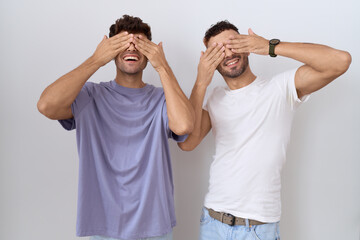 Wall Mural - Homosexual gay couple standing over white background covering eyes with hands smiling cheerful and funny. blind concept.