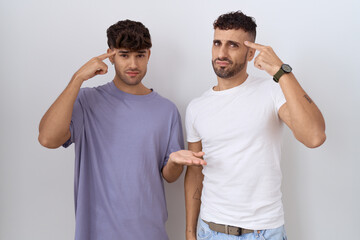 Poster - Homosexual gay couple standing over white background confused and annoyed with open palm showing copy space and pointing finger to forehead. think about it.