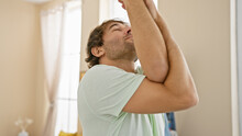 Young Caucasian Man With A Beard Stretching In A Bright Bedroom, Conveying A Relaxed Morning Routine At Home.