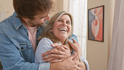 Wall Mural - Confident mother and son share a warm, smiling hug indoors, enjoying their love-filled, casual lifestyle in their happy home.