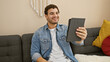 © Krakenimages.com - A smiling young man with a tablet enjoying leisure time on a sofa in a cozy living room setting.