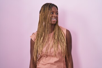 Wall Mural - African american woman with braided hair standing over pink background looking away to side with smile on face, natural expression. laughing confident.