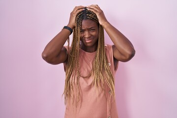 Wall Mural - African american woman with braided hair standing over pink background suffering from headache desperate and stressed because pain and migraine. hands on head.