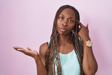 African american woman standing over pink background confused and annoyed with open palm showing copy space and pointing finger to forehead. think about it.