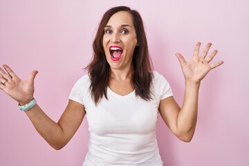 Sticker - Middle age brunette woman standing over pink background celebrating crazy and amazed for success with arms raised and open eyes screaming excited. winner concept