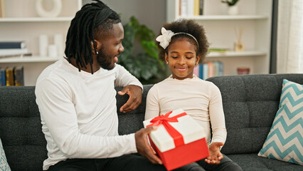 Wall Mural - African american father and daughter surprise with gift sitting on sofa smiling at home