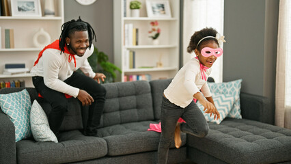 Wall Mural - African american father and daughter smiling confident wearing superhero costume playing on sofa at home