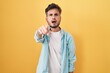 Young hispanic man with tattoos standing over yellow background pointing displeased and frustrated to the camera, angry and furious with you
