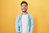 Fototapeta  - Young hispanic man with tattoos standing over yellow background sticking tongue out happy with funny expression. emotion concept.