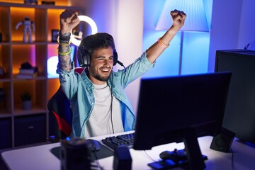 Young hispanic man streamer playing video game with winner expression at gaming room